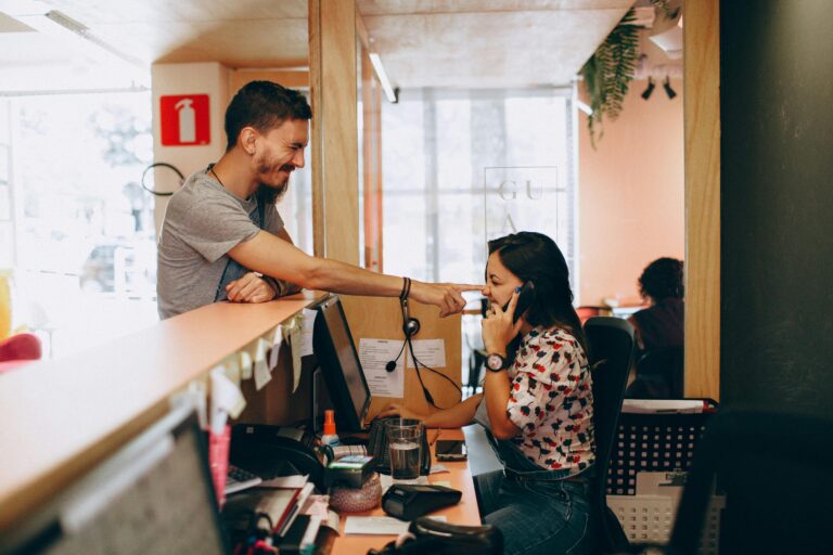 A man playfully interacts with a woman at a reception desk in a lively and modern office setting.