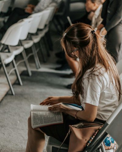 Focused woman reading a book in an academic setting with others in the background.
