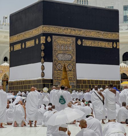 Pilgrims in white garments gather around the Kaaba in Mecca during daytime prayers.