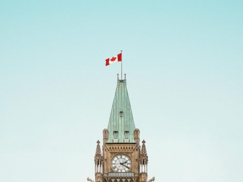 The iconic Peace Tower in Ottawa, Canada, with a clear blue sky and Canadian flag.