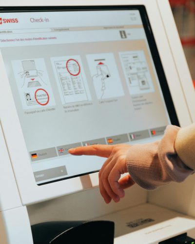 Hand interacting with airport self-service kiosk for check-in.